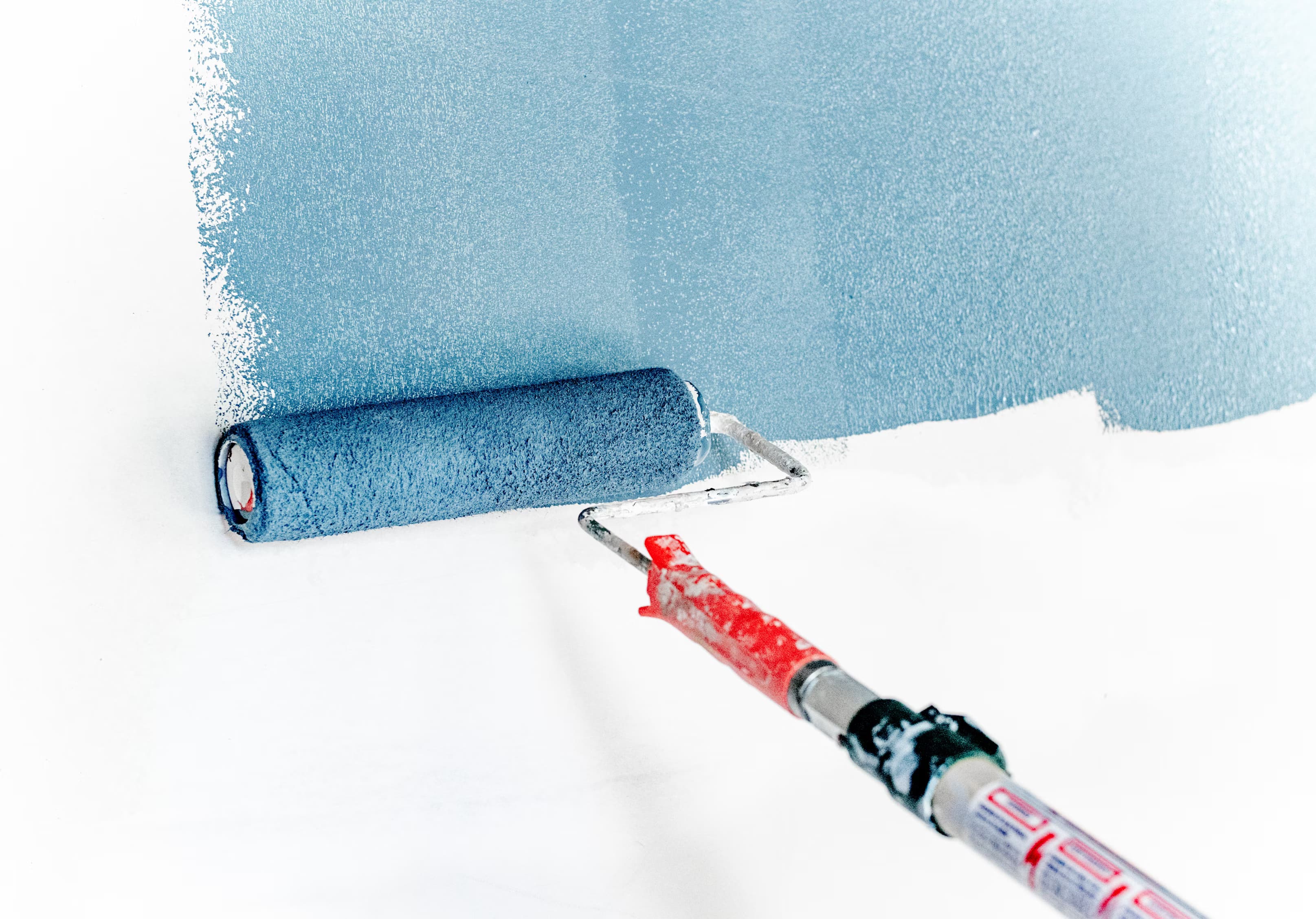 Paint roller spreading blue paint across a wall